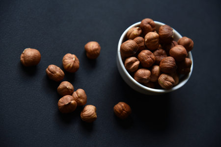 Delicious hazelnuts in a ceramic bowl on a black background. Delicious breakfast of nuts. Vegetarian...