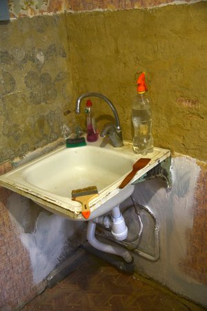 An old iron kitchen sink with a faucet in the old kitchen. Renovation in the kitchen and fresh plaster. Sink with a sanitary siphon. Design home decor. home appliance concept.の写真素材