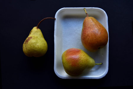 Red and green pears on a black background. Pears in a package from the store. beautiful fruits of...