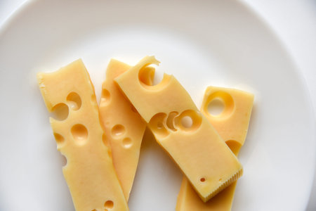Juicy pieces of yellow cheese with holes on a white plate. Delicious slices of cheese close-up....