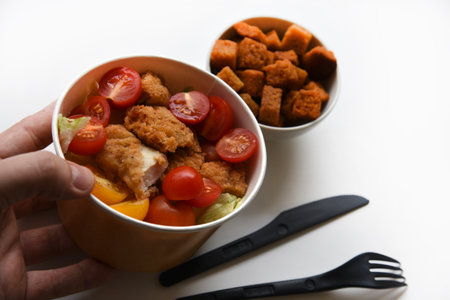 Caesar salad with tomatoes and breadcrumbs in containers. Delicious breakfast with accessories on a white background. Salad with meat and breadcrumbs.の写真素材