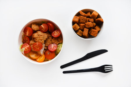 Caesar salad with tomatoes and breadcrumbs in containers. Delicious breakfast with accessories on a white background. Salad with meat and breadcrumbs.の写真素材