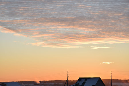 Sunset landscape in the countryside in winter. The setting sun behind the roof of the house in the evening. The disk of the sun and the evening sunset. Yellow pink beautiful sunset and sky.の写真素材