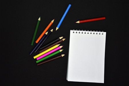 Colored pencils on a black background. Notepad and pencils.