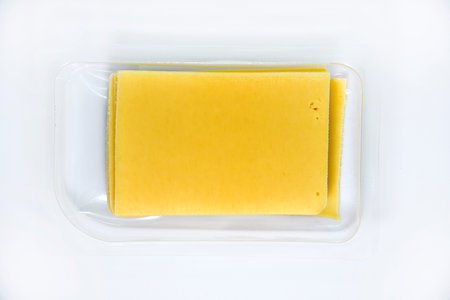 Thinly sliced slices of cheese on a plastic backing. Delicious chopped yellow cheese. Cheese in a package from the store.の写真素材