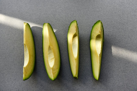 Green avocado fruit cut into slices on a white background. Avocado on a white plate. Avocado slices and halvesの写真素材