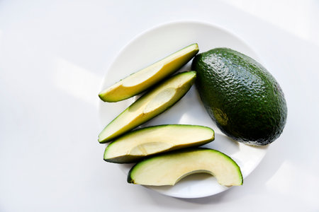 Green avocado fruit cut into slices on a white background. Avocado on a white plate. Avocado slices and halvesの写真素材