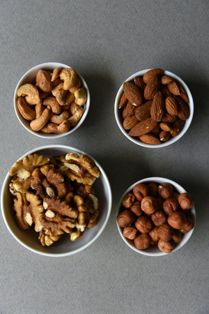 A set of nuts in white cups on a black background. Peanuts, hazelnuts and almonds. walnut. A...