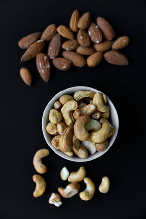 A set of nuts in white cups on a black background. Peanuts, hazelnuts and almonds. walnut. A...