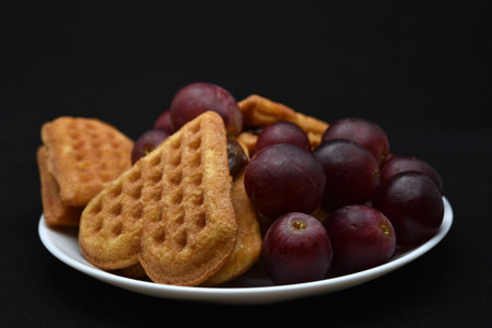 Delicious waffles and grapes on a plate. A sweet breakfast of waffles and red grapes. Heart shaped...