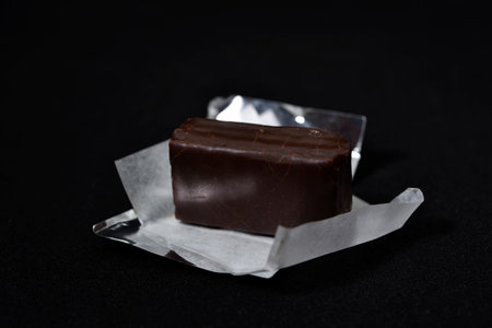 Chocolate candy in a package on a black background. sweet candy. A chocolate bar in a paper package.の写真素材