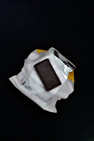 Chocolate candy in a package on a black background. sweet candy. A chocolate bar in a paper package.の写真素材
