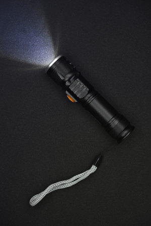 Metal black flashlight on a black background. Burning pocket flashlight close-up. lighting device.