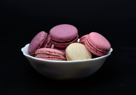 Macaroons in a white plate on a black background. Macaroons in a ceramic bowl. Colorful sweet cookies.の写真素材