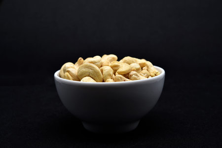 Cashew nuts in a white bowl on black background, close up