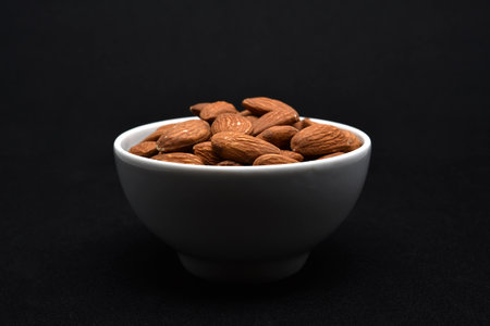 Almond nuts in a white bowl on a black background, close upの写真素材