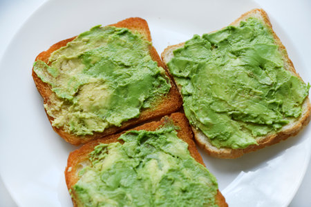 Avocado pasta on fried toast. Vegetables spread on bread. Vegan breakfast on a white plate.の写真素材