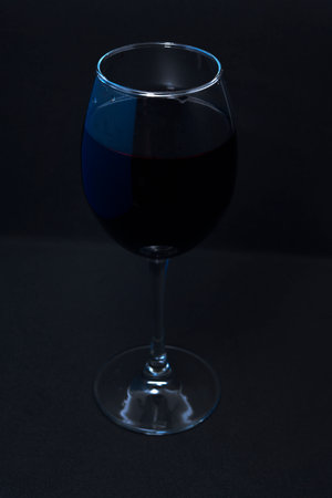 Glass wine glass on a black background. Red wine in a dark room.の写真素材