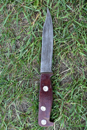 A homemade knife on the grass. An iron knife with a handle.