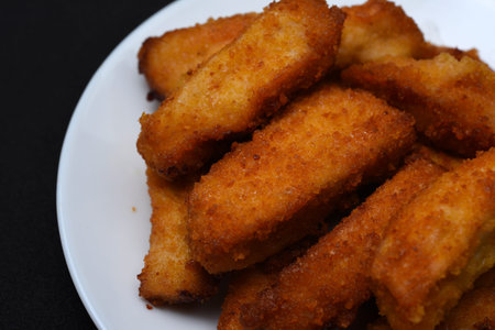 Juicy nuggets on a white plate on a black background. Chicken meat appetizer.