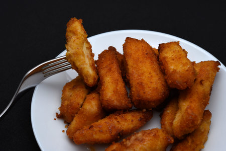 Juicy nuggets on a white plate on a black background. Chicken meat appetizer.