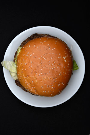 A meat burger on a white plate. A hamburger on a black background. Fast food.の写真素材