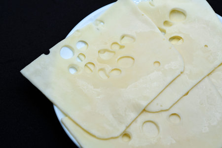 Cheese cut into flat slices on a plate. Delicious cheese.
