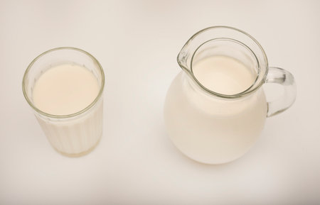 Melted milk in a milk jug and in a glass on a white background. Milk in a bowl.の写真素材