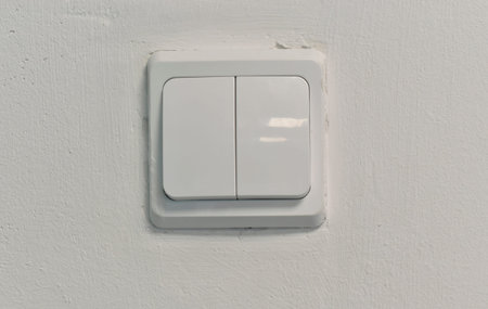 There is an electric switch on the wall. A white wall with a light switch.