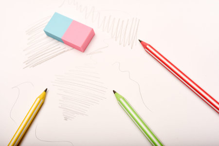 Three colored pencils and an eraser on white paper.