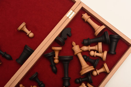 A scattering of chess pieces in a box with a red lining. A set of chess pieces. Wooden chess pieces.