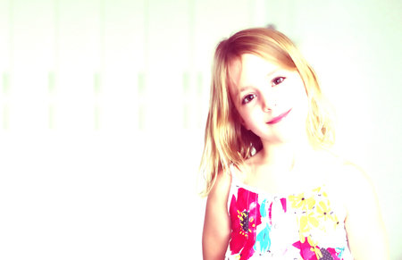 A cute six year old blonde girl in a summer white dress with flowers smiling on an abstract...