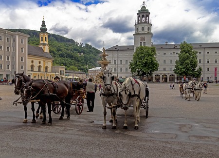 Salzburg, Austria - July15, 2017: Carriages with harnessed horses are waiting for tourists on Residence square near Salzburg Cathedral and huge fountain. Sculptor Tomasso di Garona, 1656-1661のeditorial素材