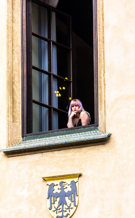 Prague, Czech Republic -July 23,2017: Young blonde woman looking from open window of medieval houses...