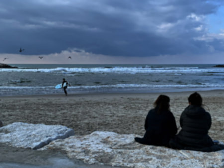 Two young women on the shore of a stormy sea. Surfer getting ready. Blurred view