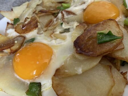 Two fried eggs with fried potatoes and green onions on a white plate on the table. Selective focusの写真素材
