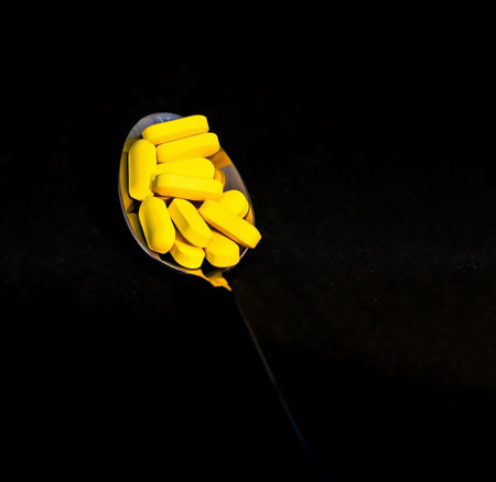 Vitamin C in spoon on black background - pharmaceutical concept. Selective focus.