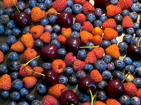 Blueberries, sweet cherry and raspberry scattered on a brown wooden table background