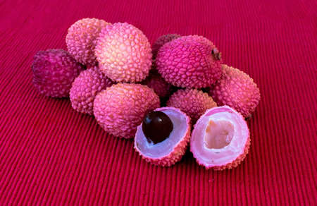 Lychee- small rounded fruit with sweet white scented flesh, a large central stone, and a thin rough skin- on red cloth napkin on table. Selective focusの写真素材