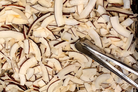 Roasted baked toasted natural thin sliced coconut chips. Background texture with white chopped...