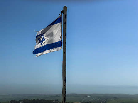 Partially torn israeli flag is waving in the wind against blue sky backgroundの写真素材