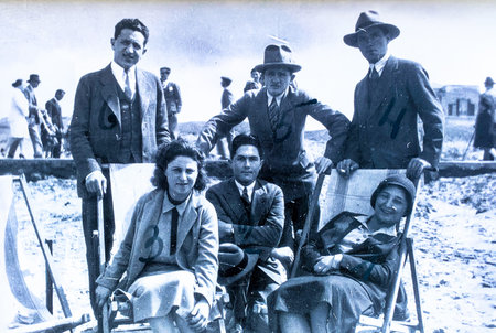 A group of well-dressed people on the Tel Aviv beach looks at the audience from a vintage photograph...