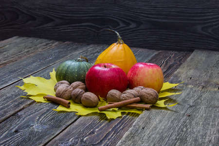 Pumpkins, apples and walnuts in the autumn leaves. Wooden dark background.の写真素材