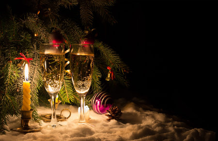 Shampane glasses and glowing candles on snow. Bells and balls on fir-tree. Copy-space.の写真素材
