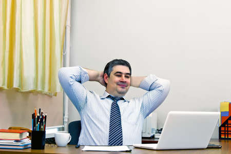 Successful mature male businessman at his desk in the office. His hands behind his head. Job satisfaction and success.の写真素材