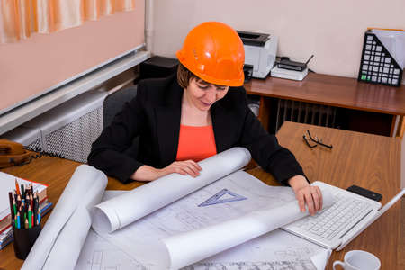 Woman builder engineer in helmet looking at blueprint paper. Construction drawing plan.の写真素材