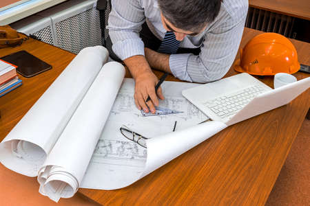Architect man working with laptop and blueprints. Engineer in workplace with architectural plan.の写真素材