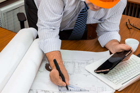 Male engineer in helmet working with a project. Marks in the drawing. Adjustment of the project.の写真素材