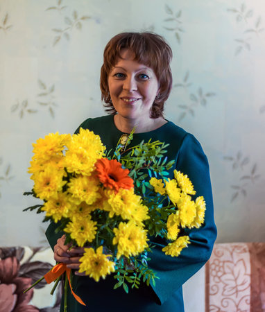 Girl in a green dress with a beautiful bouquet of flowers. Yellow chrysanthemums. The girl is smiling.の写真素材