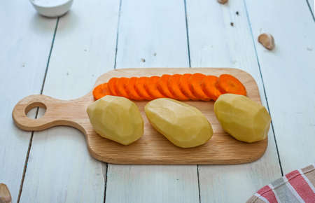 Peeled potatoes and carrots in a sliced on a cutting board. Kitchen still life.の写真素材